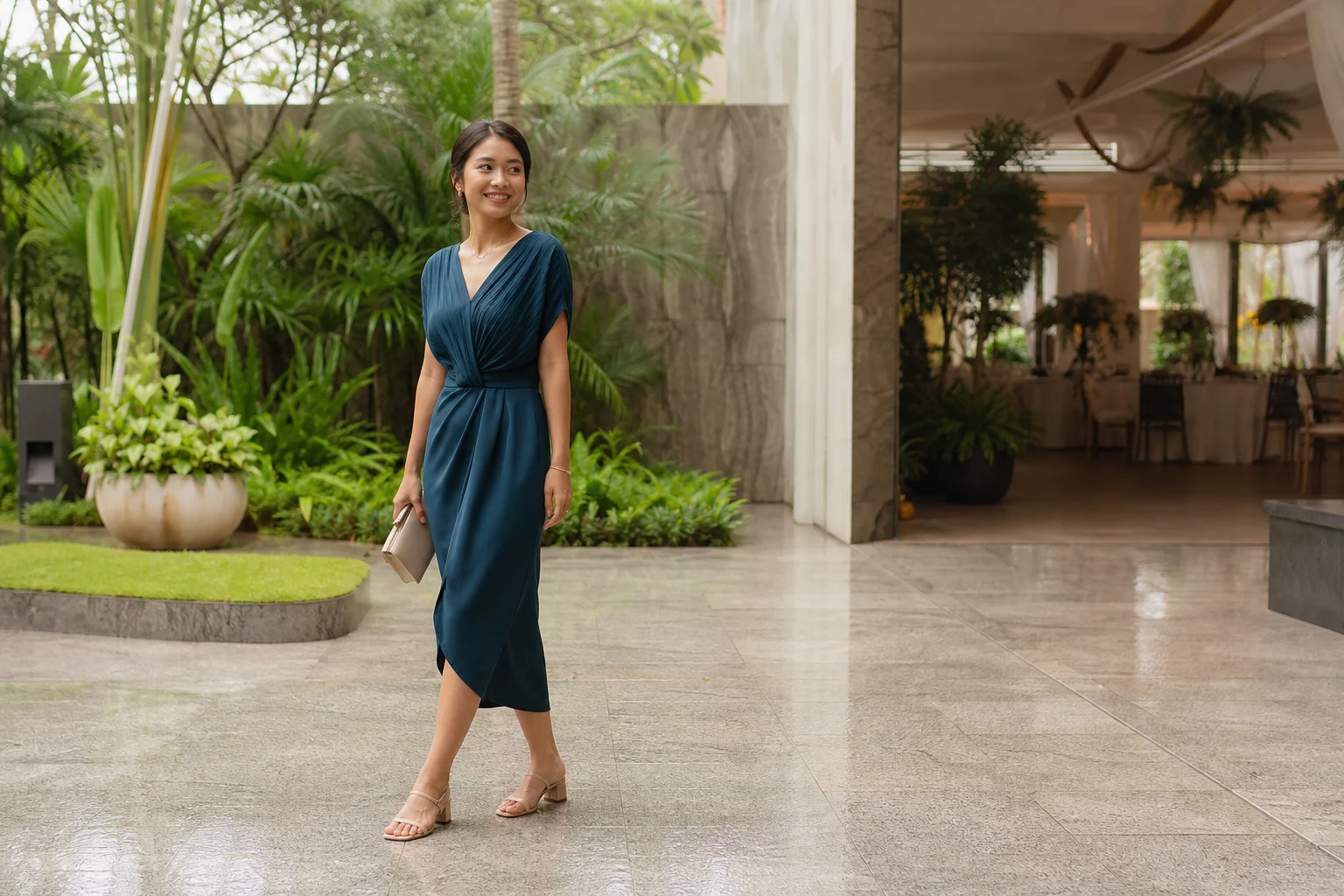 A wedding guest in a deep teal midi dress and low heels arriving at a tropical garden venue